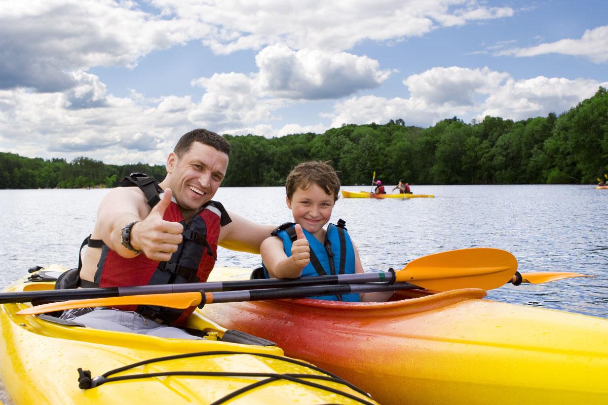 A young boy and father giving a thumbs up while in kayaks on the water.
